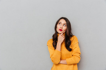 Pensive woman in sweater holding her chin and looking up