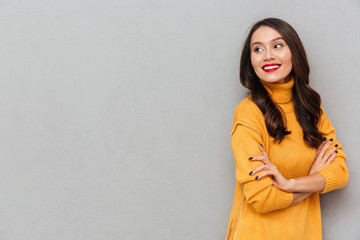 Obraz premium Pleased brunette woman in sweater with crossed arms looking away