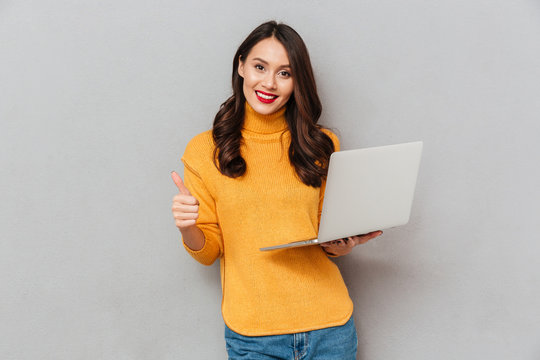 Happy brunette woman in sweater holding laptop computer