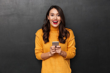Cheerful brunette woman in sweater holding smartphone