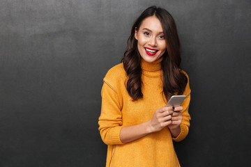 Fototapeta premium Smiling brunette woman in sweater holding smartphone