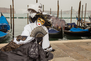 Fototapeta na wymiar Venice Carnival - Portrait of Female Venetian Mask in black and white elegant costume with venetian gondolas