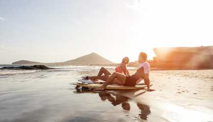 Surfers couple sitting on boards after surfing day on the beach