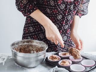 Young housewife laying the dough for the muffins in the baking dish before putting in the oven