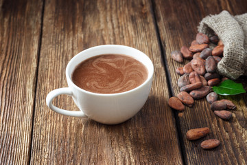 Cocoa drink in white mug and cocoa beans on wooden table.