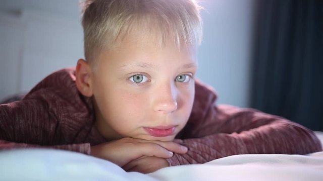 Closeup portrait of thoughtful boy laying in bed. White cute kid looks at camera.