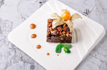 Top view piece of delicious chocolate brownie with nuts and green mint on white plate on gray background. Restaurant kitchen.