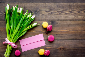 First spring flowers. Colorful tulips near envelope and macarons on dark wooden background top view copy space