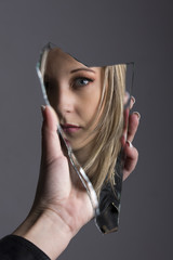 Woman looking at her face in shard of broken mirror
