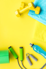 Fitness background. Equipment for gym and home. Jump rope, dumbbells, expander, mat, water on pastel yellow background top view space for text