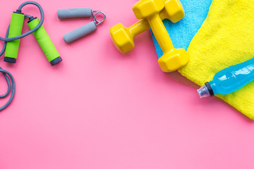 Fitness background. Equipment for gym and home. Jump rope, dumbbells, expander, water on pastel pink background top view copy space