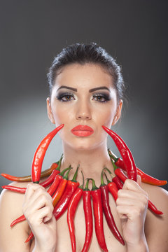 Portrait of beautiful young woman with red hot chili peppers, fashion model with creative food vegetable make up looking sideways into empty space, isolated against black background.Red chili paprika.