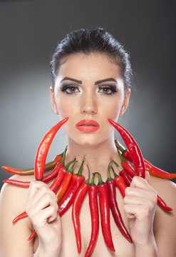 Portrait of beautiful young woman with red hot chili peppers, fashion model with creative food vegetable make up looking sideways into empty space, isolated against black background.Red chili paprika.