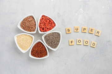 Selection of superfoods in white bowls on gray concrete background. Quinoa, chia, goji berry and flax seeds. Top view, flat lay, copy space.