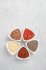 Selection of superfoods in white bowls on gray concrete background. Quinoa, chia, goji berry and flax seeds. Top view, flat lay, copy space.