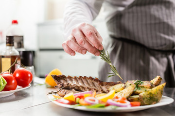 decorated with a sprig of rosemary. the chef prepares in the restaurant. Grilled rack of lamb with fried potatoes and fresh vegetables