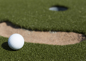 Golf ball next to a sand bunker.