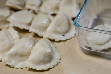 Tasty dumplings arranged on a light wooden kitchen table. Dumplings bowl and oil in the kitchen.
