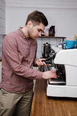 Young handsome barista hipster making coffee cafe man machine grains hot steam milk shirt cage espresso latte cappuccino