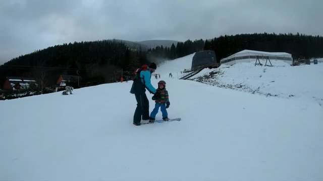 Little boy learns to ride a snowboard.
Father and son enjoy a winter day in the mountains. Stabilized video.