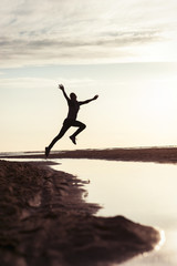 Emotions of young jumping girl silhouette in rays of sunlight at sunset.