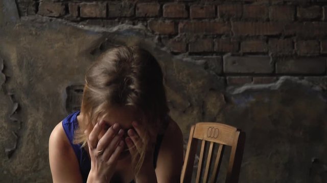 A girl with a broken face sitting on a chair pulls her hair back and embraces herself