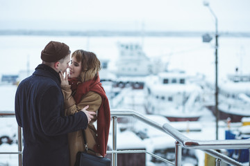 Young couple embracing at observation deck in winter city. Frozen ships in bokeh