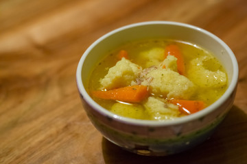 Hot chicken soup with dumplings and carrot in a small porcelain bowl on wooden table