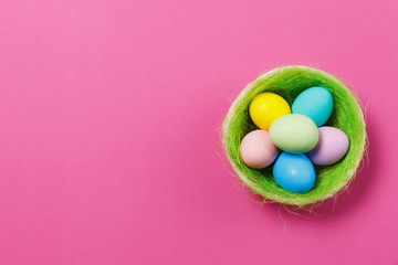 Fototapeta na wymiar Six colorful pastel monophonic painted Easter eggs in basket with green grass isolated on pink background. Happy Easter concept. Copy space for advertisement. With place for text. Top view on eggs.