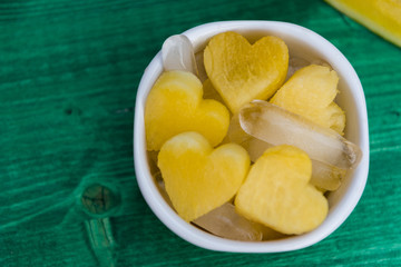 Sweet honey yellow watermelon heart shaped pieces, served with ice in white bowl, on green background