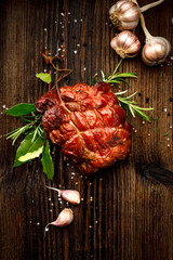 Smoked gammon on a wooden rustic table with addition of fresh aromatic herbs, top view.  Natural product from organic farm, produced by traditional methods