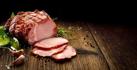 Sliced smoked gammon  on a wooden  table with addition of fresh  herbs and aromatic spices.   Natural product from organic farm, produced by traditional methods - obrazy, fototapety, plakaty