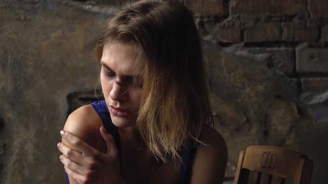 A girl with wounds received sits on a chair and closes her eyes from pain