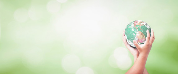 Earth Day concept: Two human hands holding earth globe over green forest background. Elements of this image furnished by NASA.