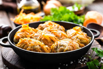 Cabbage rolls stewed with meat and vegetables in pan on dark wooden background