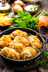 Cabbage rolls stewed with meat and vegetables in pan on dark wooden background