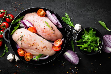 Fresh raw chicken meat, fillet marinated with spices, onion and tomatoes on black background. Top...