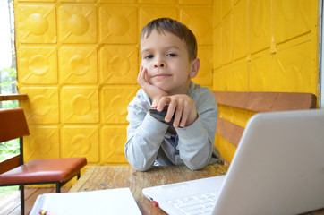 Naklejka premium A teenager is sitting at a table in front of a laptop. the boy looks seriously at the computer. working. Outdoors. in the arbor, in the village