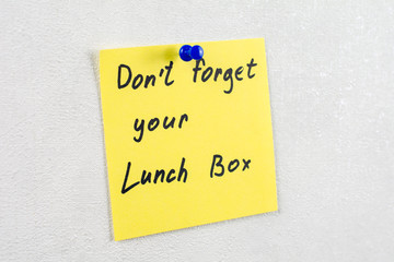 don't forget your lunch box  note reminder yellow sticker on a white wall pinned with blue pushpin, close up, selective focus