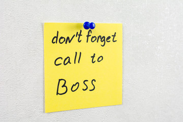 don't forget call to boss note reminder yellow sticker on a white wall pinned with blue pushpin, close up, selective focus