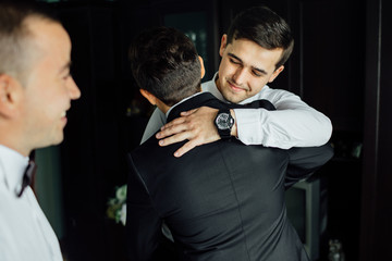 stylish groomsmen helping happy groom getting ready in the morning for wedding ceremony.