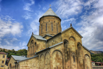 Fototapeta na wymiar Ancient georgian cathedral on mountains and clouds background at sunny day