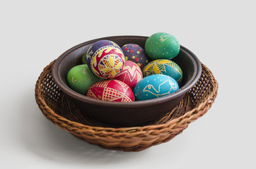 colorful painted Easter eggs in a woven straw basket isolated on white background