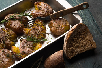 Baked potatoes cooked in baking tray with herbs, salt, oil and spices. Step homemade recipe. Food dark wooden background.
