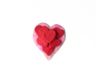 Beautiful several red hearts are placed on a pink heart handmade from plasticine clay are on white background,cute shape dough