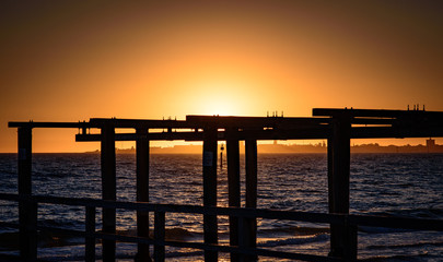 Fototapeta na wymiar The sun sets over the horizon of Port Phillip Bay with a silhouetted wooden boat launch structure in the foreground. Melbourne Australia