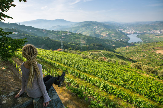 Vineyards on a hills. Young woman with blond dreadlocks on the edge of a cliff and looks down at on the Douro Valley, Portugal.
