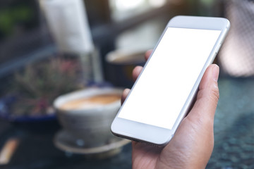 Mockup image of a woman's hand holding white mobile phone with blank desktop screen and coffee cup in cafe