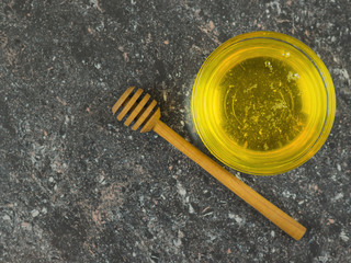 Honey in a glass bowl with a wooden spoon on black stone table. Fresh harvest of honey.