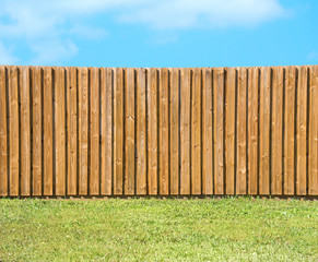 Generic wooden residential privacy fence with  a lush green grass yard in the foreground and a beautiful blue sky with fluffy clouds. - 188769184